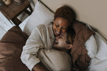 Happy non-binary couple laughing together while lying on bed at home - MASF37041