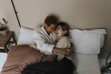 Non-binary couple enjoying with each other while lying on bed at home - MASF37042