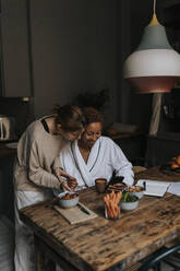 Non-binary couple sharing smart phone while having breakfast at home - MASF37083