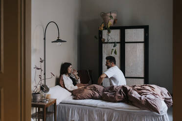 Couple talking to each other while sitting on bed at home - MASF37091