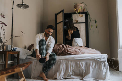 Man wearing sock with non-binary person standing near wardrobe in bedroom at home - MASF37100