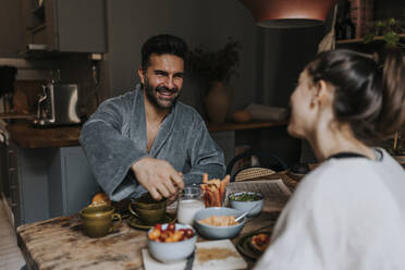 Happy man enjoying breakfast with non-binary person at home - MASF37114