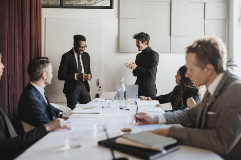 Happy male entrepreneurs discussing during business meeting at office - MASF37125