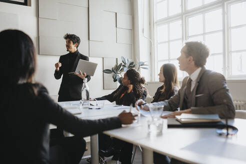 Businessman holding laptop and explaining colleagues in meeting at office - MASF37128