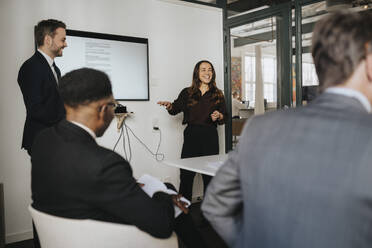 Female entrepreneur discussing over presentation with colleagues in board room at office - MASF37138