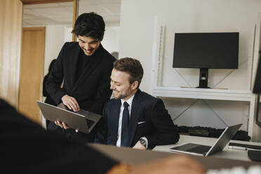 Smiling businessman explaining male colleague over laptop at office - MASF37146