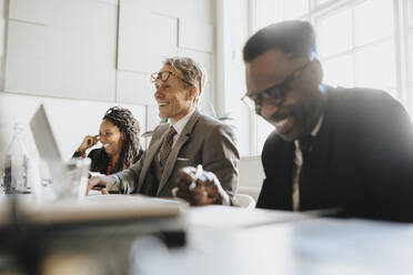 Smiling mature entrepreneur with male and female colleagues during meeting at office - MASF37149