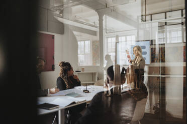 Businesswoman discussing over presentation with male and female colleagues in board room at office - MASF37161