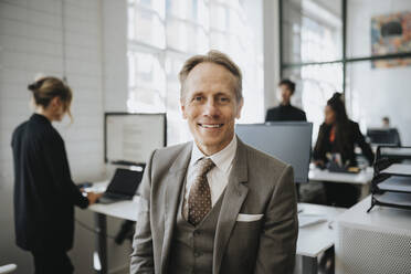 Portrait of smiling mature businessman wearing suit at office - MASF37175