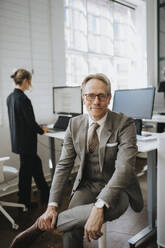 Portrait of smiling businessman wearing eyeglasses sitting at office - MASF37176