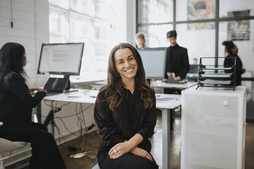 Portrait of smiling businesswoman sitting at corporate office - MASF37178