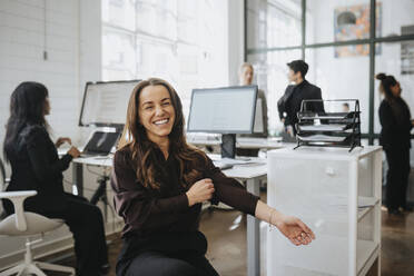 Happy businesswoman pulling sleeve while sitting at office - MASF37180