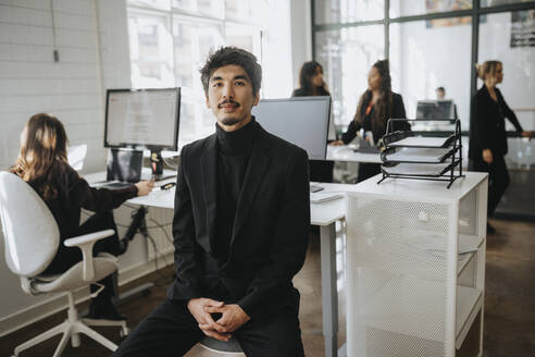 Portrait of businessman sitting with hands clasped sitting at office - MASF37186