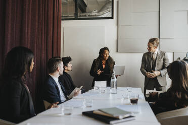 Female entrepreneur discussing with male and female coworkers during business meeting at office - MASF37190