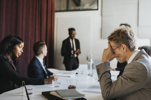 Side view of businessman with head in hand during meeting with colleagues in board room at office - MASF37201