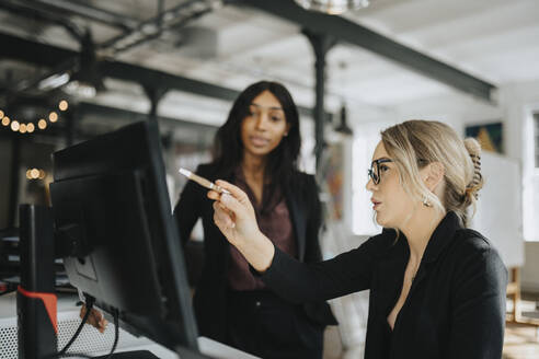 Young businesswoman explaining female colleague over desktop PC at office - MASF37202