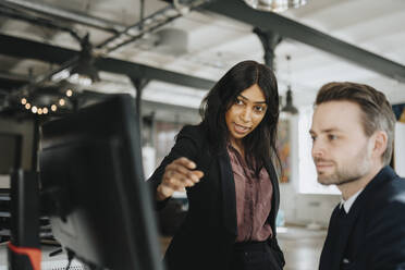 Female entrepreneur explaining male coworker over desktop PC at office - MASF37203