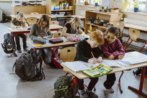 Männliche und weibliche Studenten, die zusammen am Schreibtisch im Klassenzimmer sitzen - MASF37215