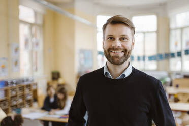 Portrait of smiling male teacher with stubble in classroom - MASF37219