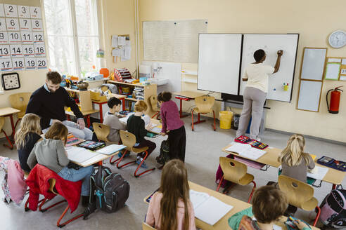 Male and female teacher teaching pupils sitting at desk in classroom - MASF37225