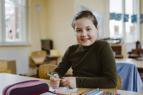 Portrait of smiling female pupil sitting at desk in classroom - MASF37227