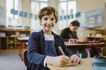 Portrait of smiling schoolboy sitting at desk in classroom - MASF37231