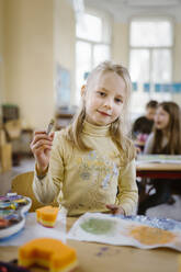 Portrait of female blond student holding paintbrush in classroom - MASF37234