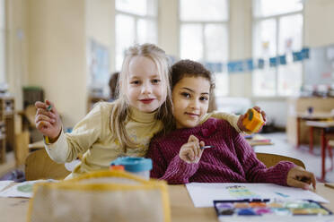 Portrait of schoolgirl with arm around female friend in classroom - MASF37235