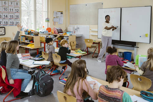 Female teacher talking to male and female pupils during lecture in classroom - MASF37240