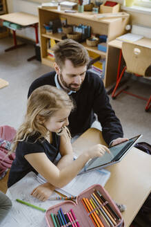 Girl studying through tablet PC by male teacher in classroom - MASF37243