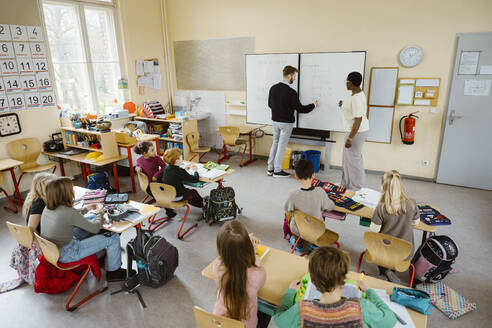 Male and female teachers solving maths problem in front of students in classroom - MASF37262