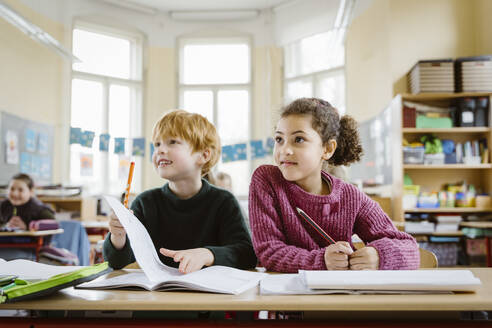Smiling blond boy sitting with girl at desk looking away in classroom - MASF37265