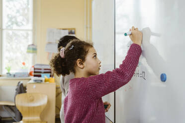 Side view of girl and boy writing on whiteboard in classroom - MASF37270