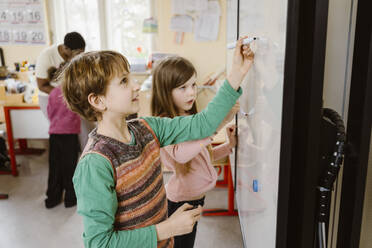 Boy writing on whiteboard while solving maths problem by girl in classroom - MASF37274