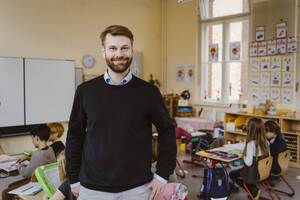 Portrait of smiling bearded teacher standing in front of students at classroom - MASF37278