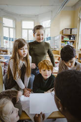 Boys and girls looking at teacher helping them in classroom - MASF37283