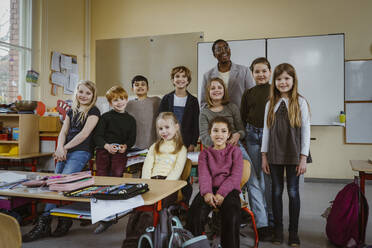 Portrait of smiling teacher and boys and girls against whiteboard in classroom - MASF37287