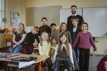 Portrait of smiling teacher and girls and boys against whiteboard in classroom - MASF37288