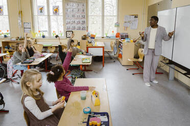 Teacher standing by whiteboard while asking questions to students in classroom - MASF37292