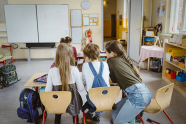 Rear view of boy and girls studying together at desk in classroom - MASF37297