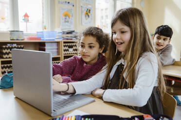 Schoolgirls using laptop together at desk in classroom - MASF37298