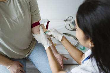 High angle view of doctor piercing needle in patient's arm for medical exam in clinic - MASF37310