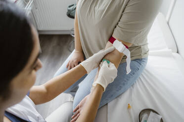 Doctor wearing glove piercing needle in patient's arm at clinic - MASF37311