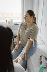 Female patient doing medical checkup while sitting on bed in clinic - MASF37312