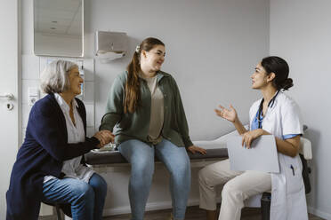 Female doctor explaining patient sitting with mother in clinic - MASF37322