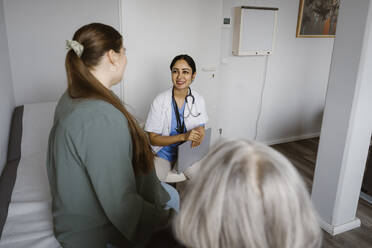 Smiling doctor discussing with patient sitting in consulting room - MASF37323