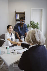 Smiling doctor shaking hands with senior patient in clinic - MASF37337