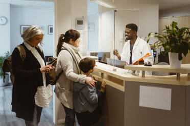 Patients standing and talking to male receptionist through transparent shield in clinic - MASF37356