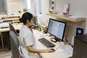 Female healthcare worker using computer while talking on smart phone at clinic - MASF37362