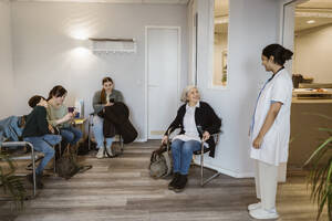 Female healthcare worker communicating with patients sitting in waiting room at healthcare center - MASF37374
